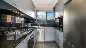A modern kitchen with stainless steel appliances, a dishwasher, and a window providing a view of the outdoors. - Garran Treetop Views - Balcony & Mountain Sunsets (Garran)