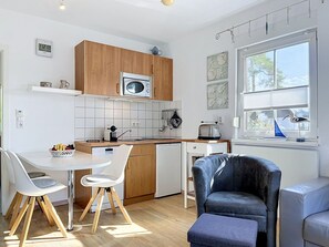 Cozinha compacta com micro-ondas, torradeira e pia. Conta com uma área de refeições com mesa e cadeiras.