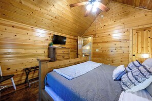 Ein Schlafzimmer einer Holzhütte mit einem Bett, einem Fernseher, einem Schminktisch und einer Bank.