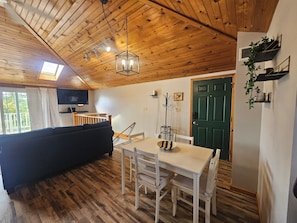 A cozy room with a wooden ceiling, a dining table with chairs, a sofa, a television, and a green door. - Okauchee Lakefront Escape with Amazing Sunsets, Fire Pits, Deck & Pet Friendly (Nashotah)