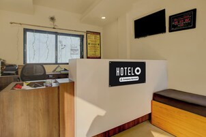 Un mostrador de recepción de hotel con un letrero que indica servicio de empresa. Se ve una ventana con vistas a un edificio y una decoración con motivos de pavo real.