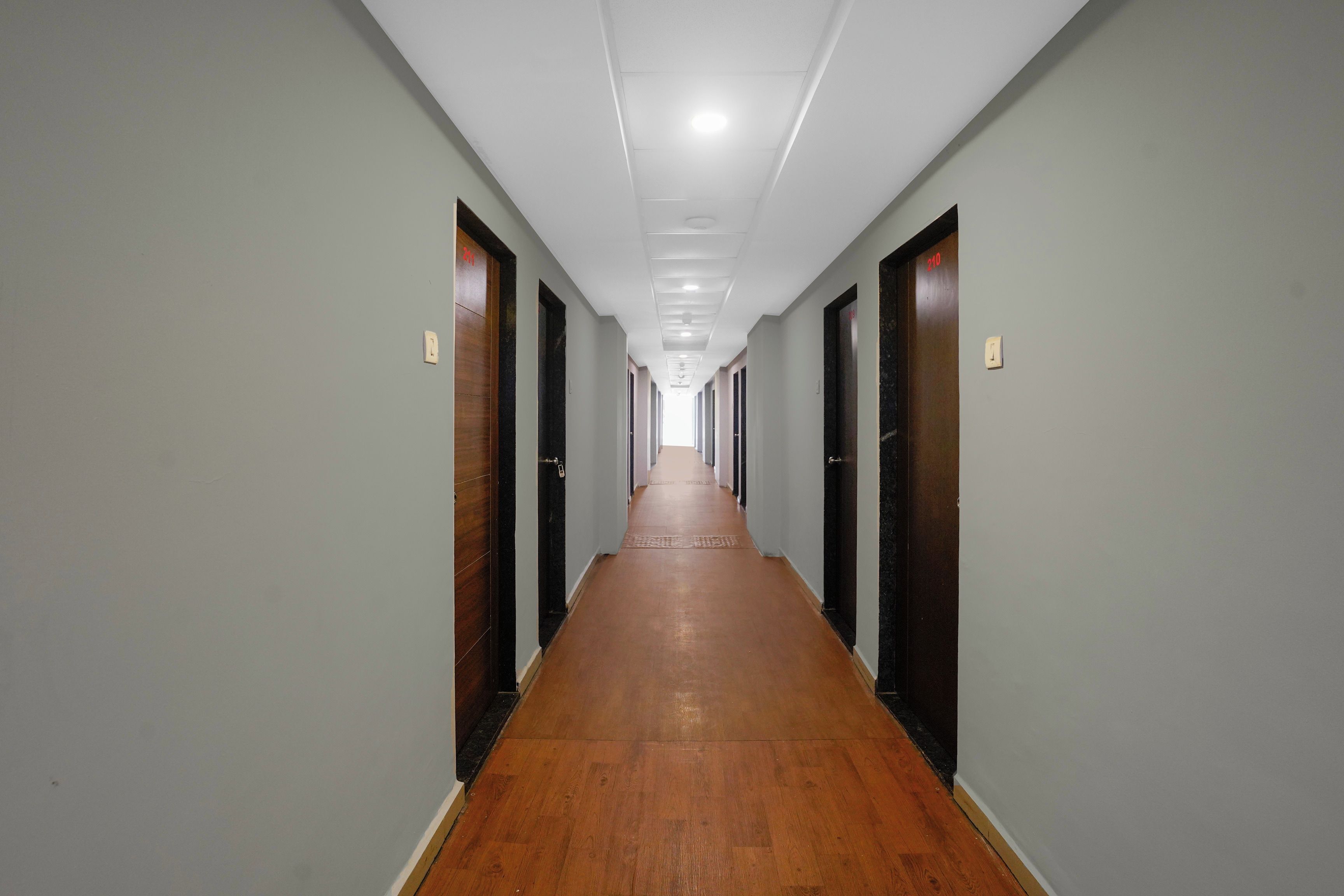 A long, narrow hallway with wooden flooring and doors on both sides, leading to a bright room at the end.