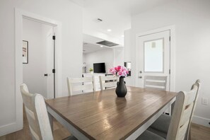 A dining area with a wooden table, white chairs, a vase with flowers, and a television in the background. - Private 3BR 2.5BA Home | Sleeps 9 | Fire Pit, BBQ + Fenced Yard | 15 Min to ATX (Austin)