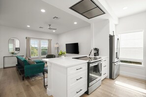 A modern kitchen with a central island, built-in oven, and a flat-screen TV. - Private 3BR 2.5BA Home | Sleeps 9 | Fire Pit, BBQ + Fenced Yard | 15 Min to ATX (Austin)