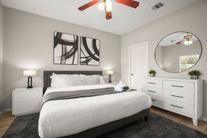 A bedroom with a bed, bedside tables, a dresser, a mirror, and abstract wall art. - Private 2BR Guest House | Sleeps 9 | BBQ + Fenced Yard | 12 Min to Airport (Austin)
