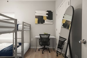 Ein Schlafzimmer mit einem Etagenbett, einem Schreibtisch mit Stuhl und einem großen Spiegel.