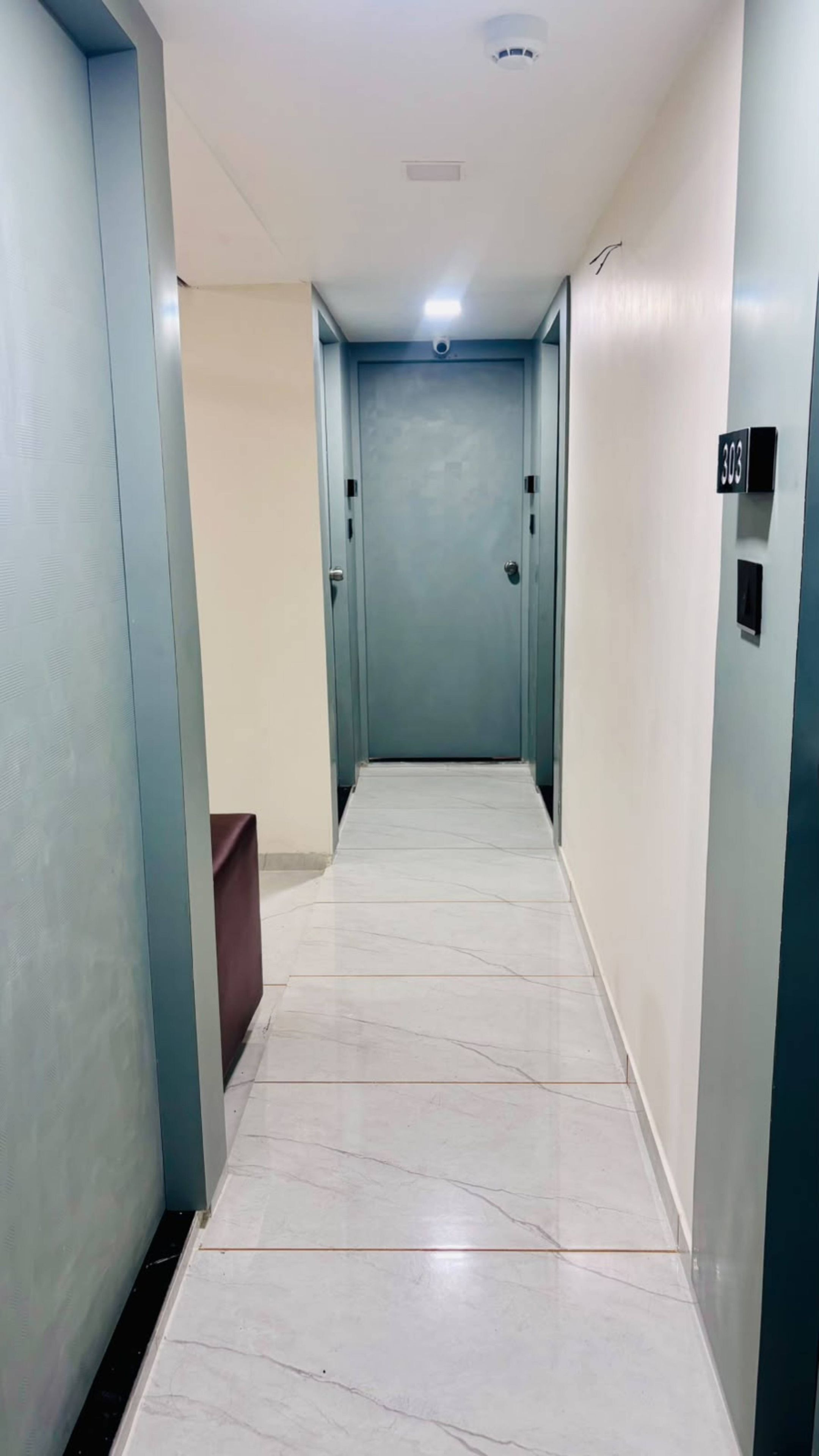 A corridor with a marble floor, light blue walls, and a door at the end.