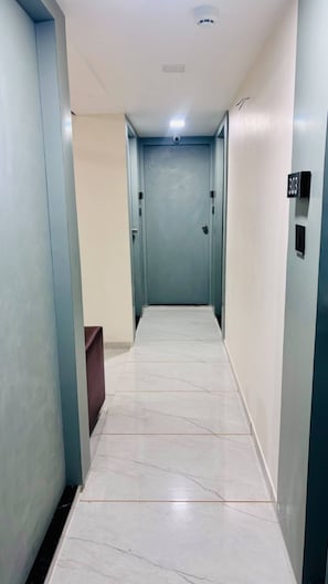 A corridor with a marble floor, light blue walls, and a door at the end. - Hotel Blue City (Ahmedabad)