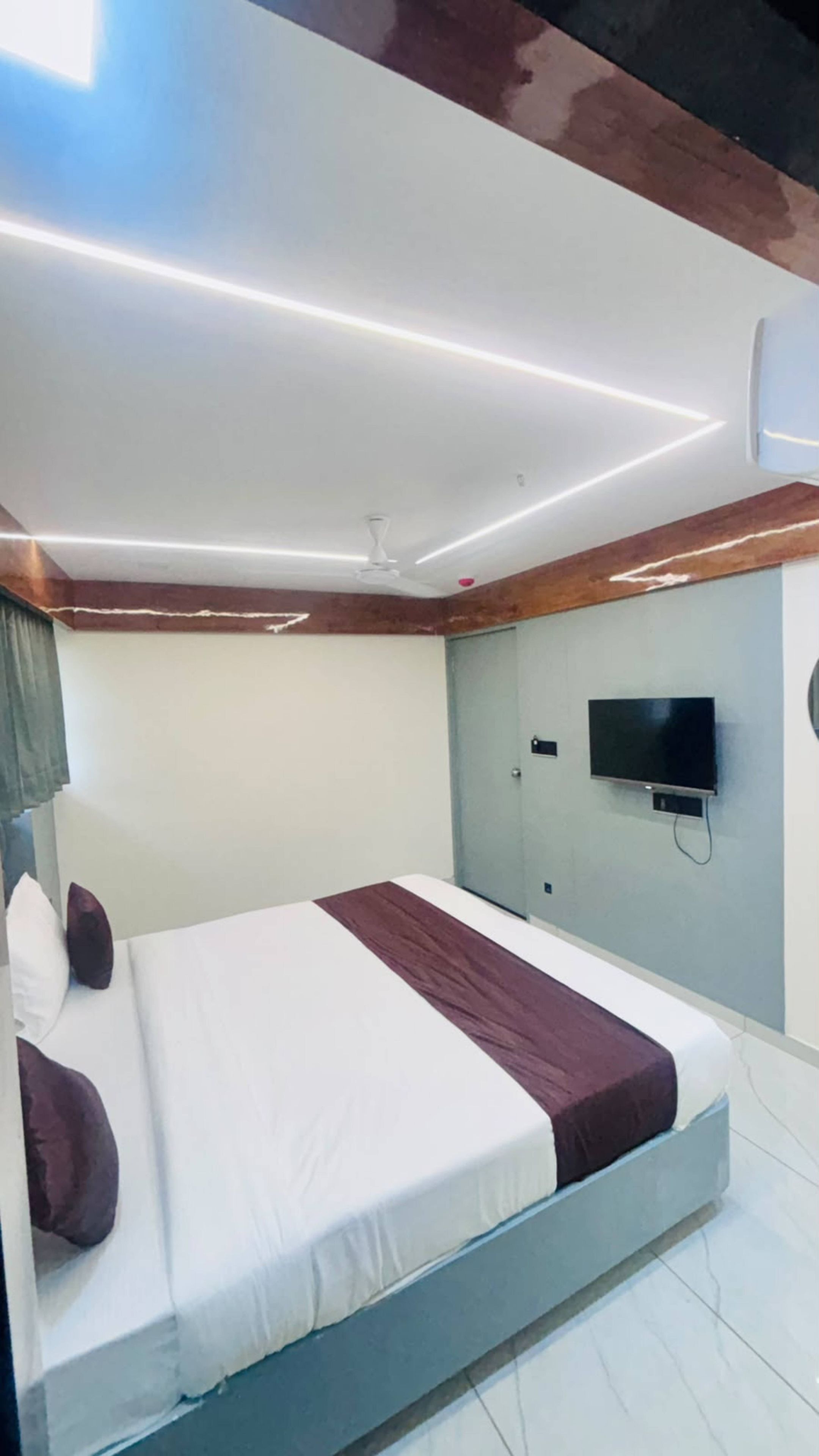 Hotellihuone, jossa on sänky, seinälle asennettu taulutelevisio ja kattotuuletin.