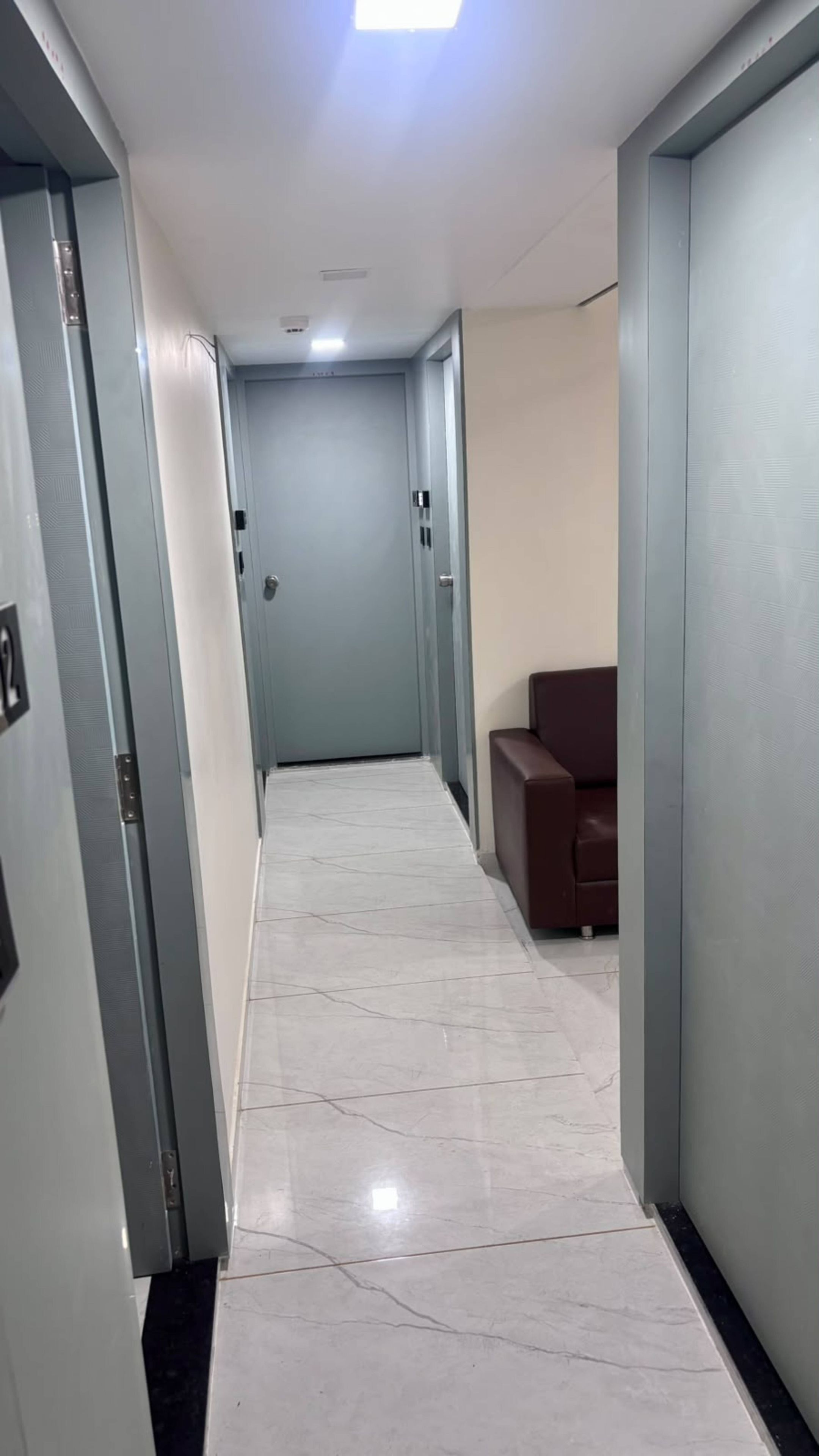 A hallway with a tiled floor, a door at the end, and a brown chair to the right.