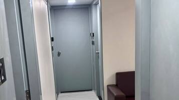 A hallway with a tiled floor, a door at the end, and a brown chair to the right.