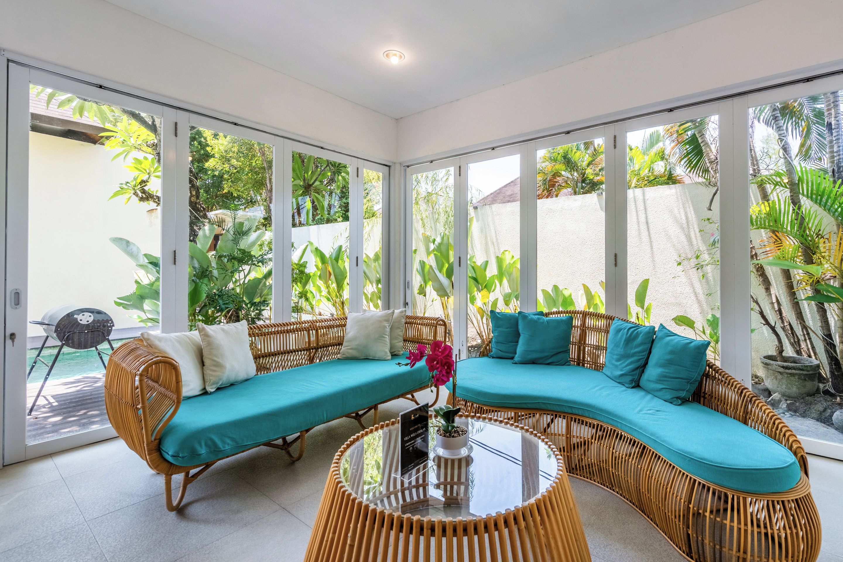 A room with a curved sofa set, a glass coffee table, and large windows offering a view of greenery outside.