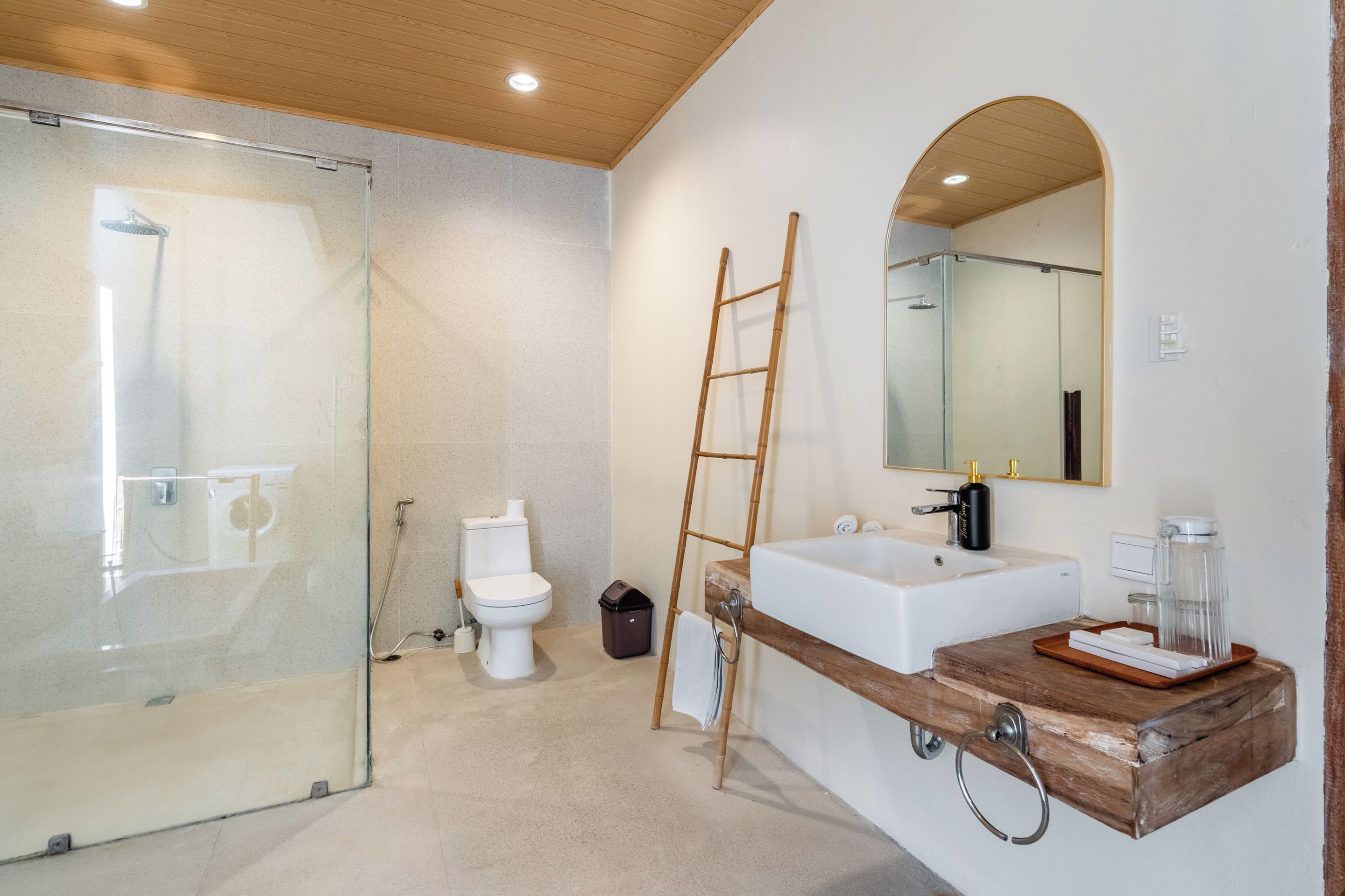 Un baño moderno con cabina de ducha de vidrio, inodoro blanco, tocador de madera con lavamanos y un espejo.