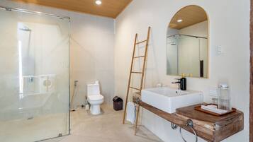 Un baño moderno con cabina de ducha de vidrio, inodoro blanco, tocador de madera con lavamanos y un espejo.