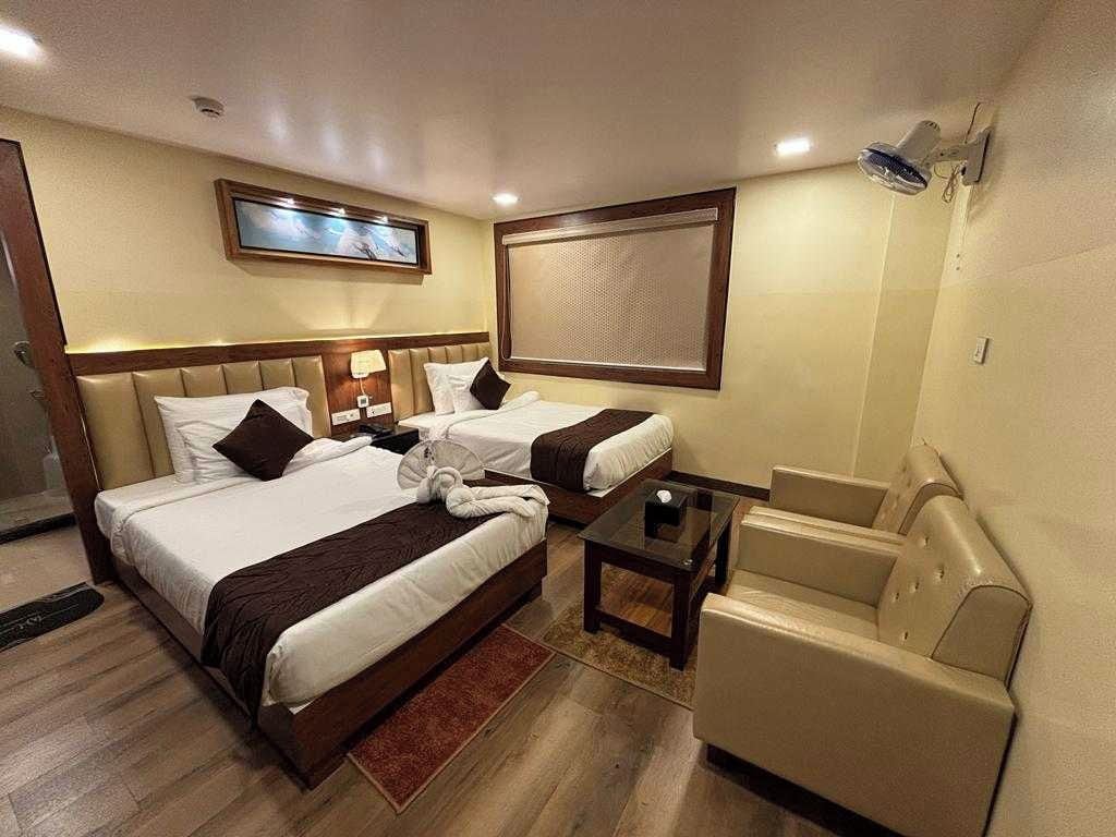 A hotel room with two beds, a sofa, a small table, and a TV mounted on the wall.