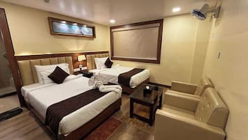 A hotel room with two beds, a sofa, a small table, and a TV mounted on the wall.