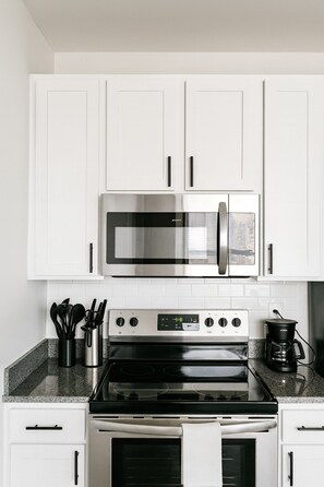 A modern kitchen with white cabinetry, a stainless steel oven, a microwave, and a gas stove. - Luxury 2BR Condo | Steps from UAB Campus 61 5F (Birmingham)