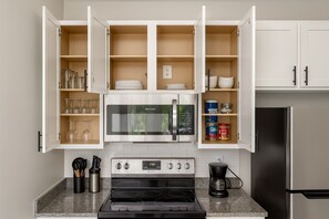 Une cuisine moderne avec des meubles blancs, un réfrigérateur en acier inoxydable, un four à micro-ondes, un four et une machine à café.