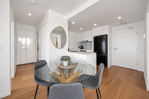 A modern kitchen with white cabinets, a black refrigerator, and a glass dining table with chairs. - Walk to King St & RBWH | Parking (Bowen Hills)