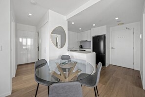 A modern kitchen with a black refrigerator, white cabinets, and a round glass table with chairs. - Walk to King St & RBWH | Parking (Bowen Hills)
