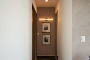 Un corridoio con un lampadario, due quadri appesi al muro e un interruttore a destra.