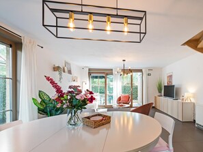 A modern dining area with a round table, a vase of flowers, and a chandelier.