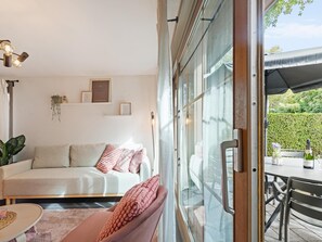 A modern living room with a sofa, a glass door leading to an outdoor area, and a table with a bottle and glass.