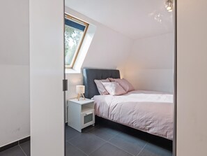 A bedroom with a bed, a nightstand, a lamp, and a skylight.