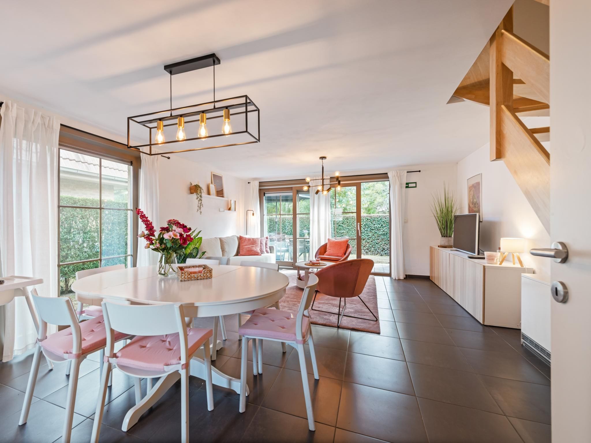 Un interior moderno con una mesa de comedor redonda, sillas blancas, un sofá y una escalera.