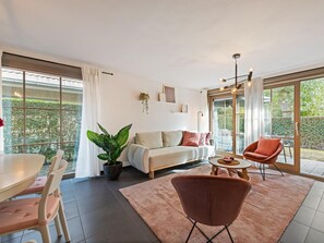 Una sala de estar moderna con sofá, mesa de centro y sillas, una mesa de comedor con sillas, y ventanas grandes con cortinas.