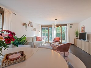 A modern living room with a sofa, chairs, a dining table, and a TV.