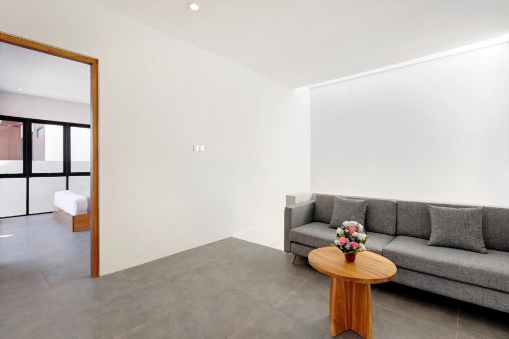 A modern living room with a grey sofa, a round wooden coffee table with a flower vase, and a wooden floor.