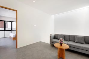 A modern living room with a grey sofa, a round wooden coffee table with a flower vase, and a wooden floor.