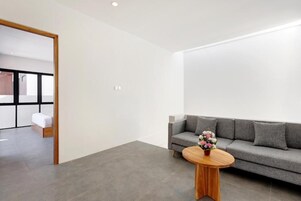 Una sala de estar moderna con un sofá gris, una mesa de centro redonda de madera y un suelo de madera.