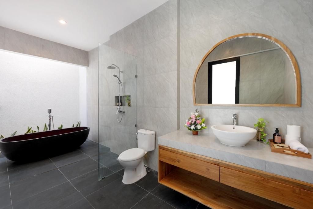 A modern bathroom with a freestanding bathtub, a toilet, a sink with a large mirror, and a shower area.