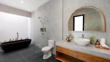 A modern bathroom with a freestanding bathtub, a toilet, a sink with a large mirror, and a shower area.