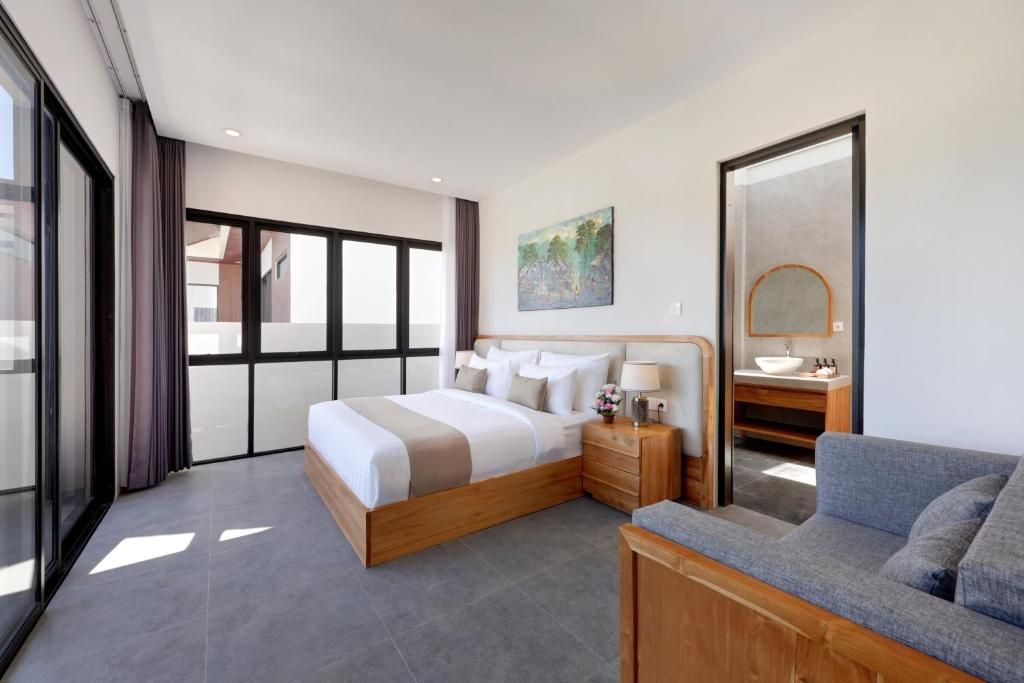 A modern bedroom with a large bed, bedside tables, a sofa, and a bathroom with a sink and mirror.