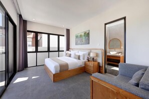 Un dormitorio moderno con una cama grande, mesitas de noche, un sofá y un baño con lavamanos y espejo.