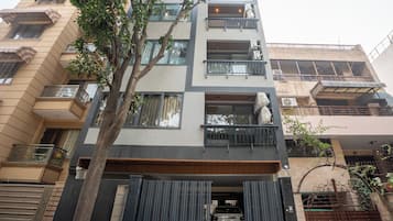 A multi-story residential building with balconies, a gated entrance, and a tree in the foreground.