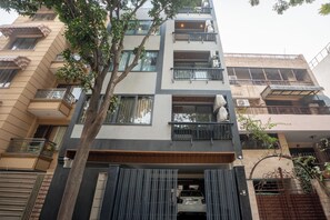 A multi-story residential building with balconies, a gated entrance, and a tree in the foreground.