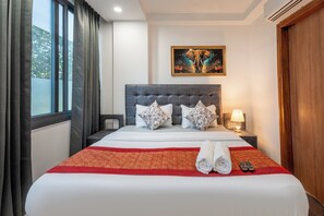 Une chambre d’hôtel avec un grand lit, une tête de lit, un tableau au mur et une fenêtre avec des rideaux.
