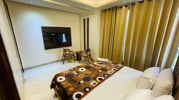 Habitación de hotel con cama, televisión de pantalla plana en la pared, ventilador de techo y ventana con cortinas.