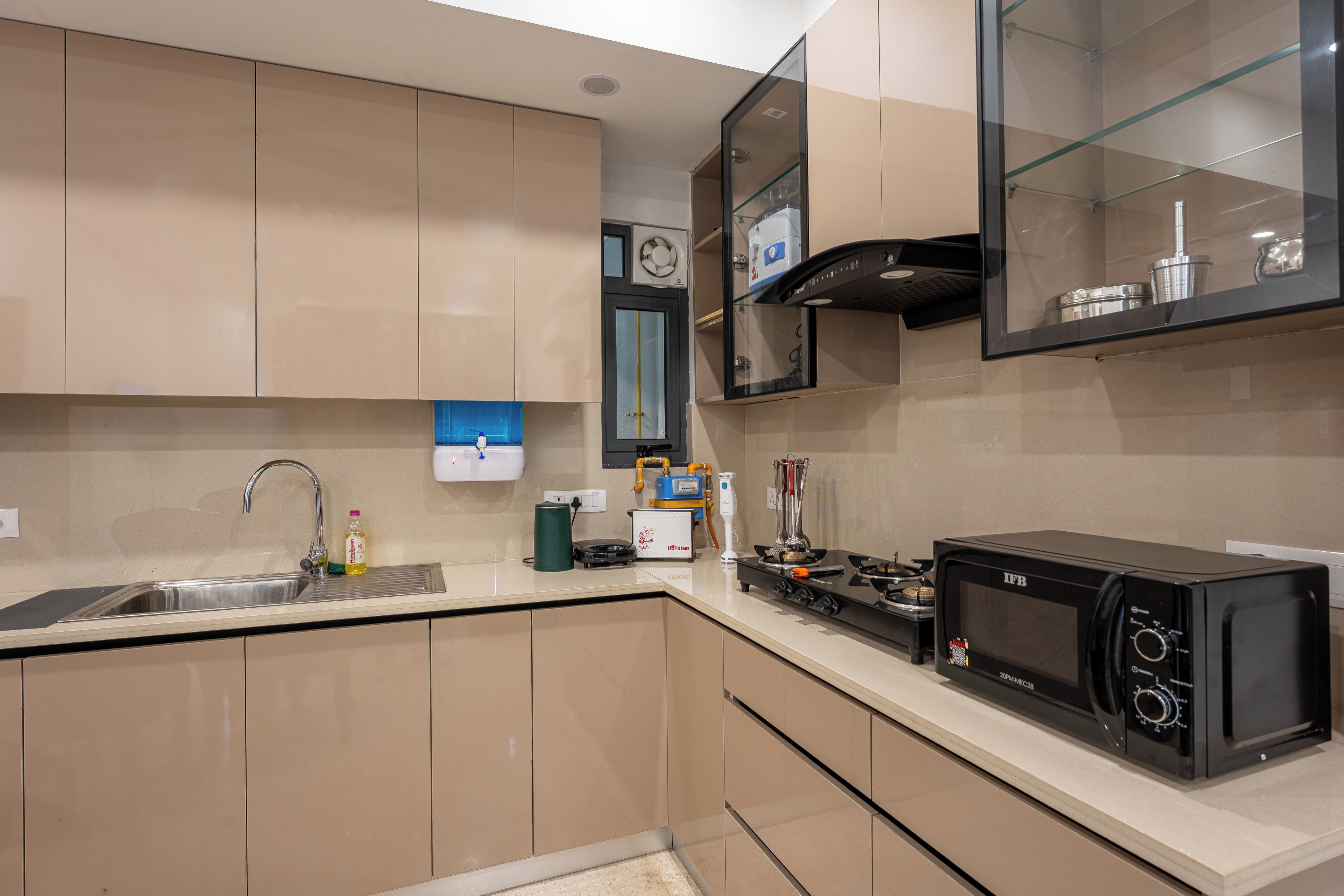 A modern kitchen with beige cabinets, a stainless steel sink, a black microwave, and a gas stove.
