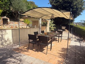 Une terrasse extérieure avec une table et des chaises, une pergola offrant de l’ombre et un mur de pierre agrémenté de plantes.