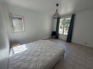 A bedroom with a bed, a window with curtains, a chair, and a hanging light fixture. - Family home with a terrace in a quiet neighborhood in Pégomas (Pégomas)