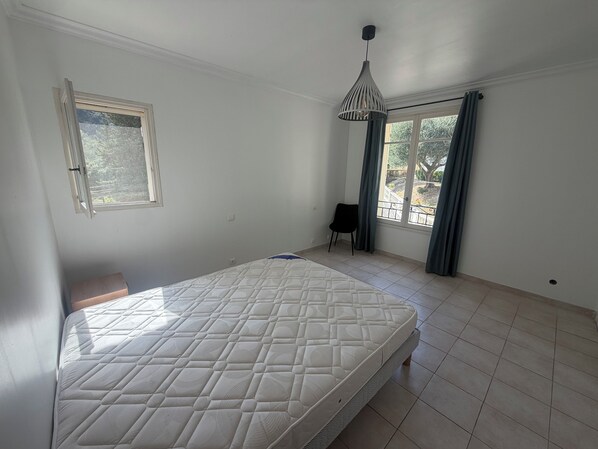 Une chambre à coucher avec un lit, une fenêtre avec des rideaux, une chaise et un luminaire suspendu.