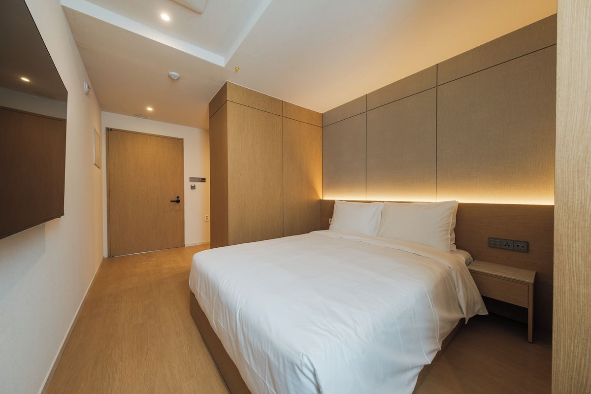 A modern hotel room with a large bed, a bedside table, and a built-in headboard.