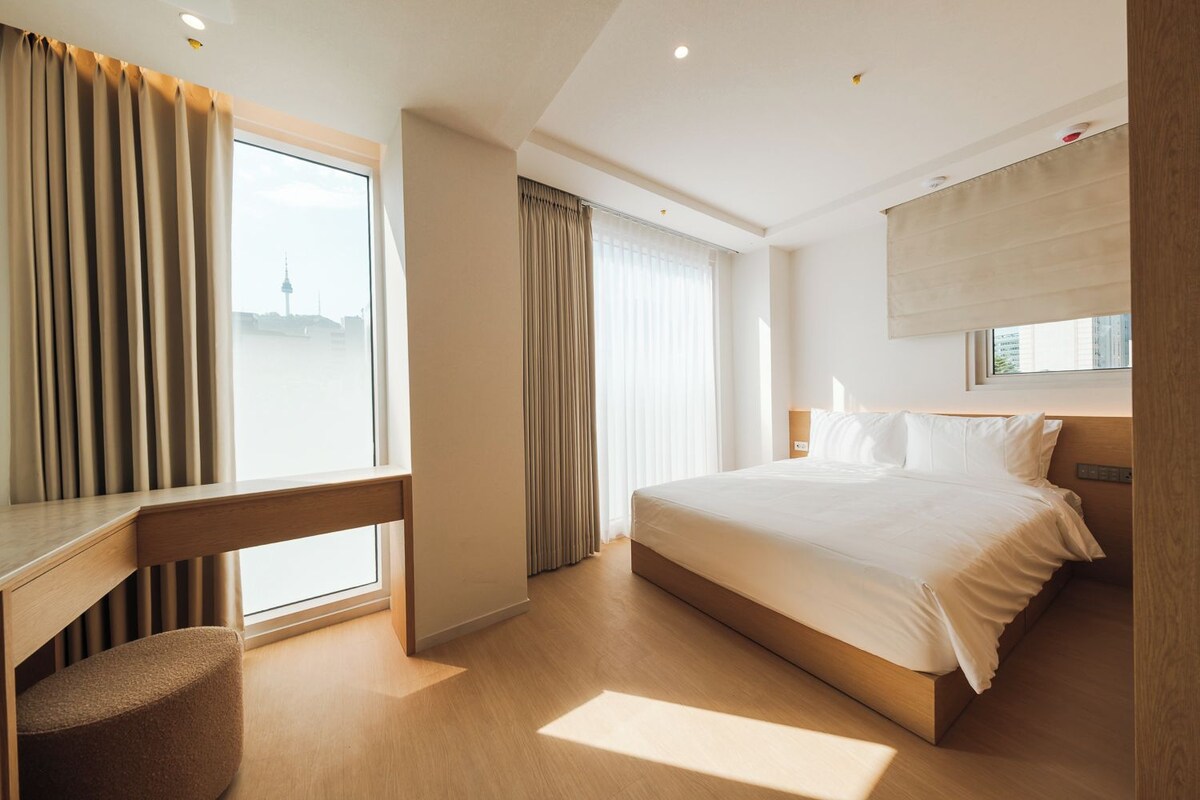 A hotel room with a bed, a desk, and a window with curtains.