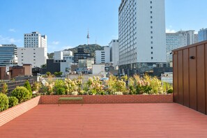 A rooftop terrace with a brick wall and a wooden deck, overlooking a cityscape with modern buildings and a hill with a tower. - Nori Hotel (Seoul)