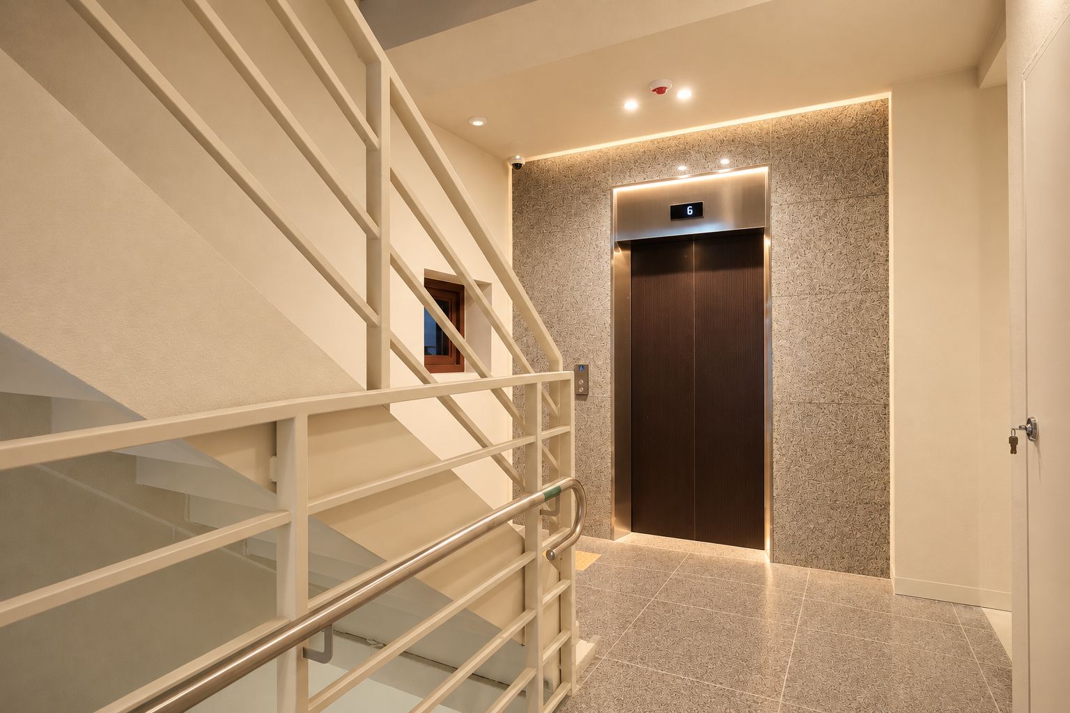 Un ascenseur moderne doté d’un écran numérique, un escalier en verre avec des rampes métalliques et un mur à texture.